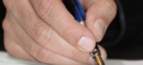 Ręka osoby trzymająca długopis nad kawałkiem papieru na biurku z przyborami biurowymi. Pisanie z nadgarstkiem opartym na stole.