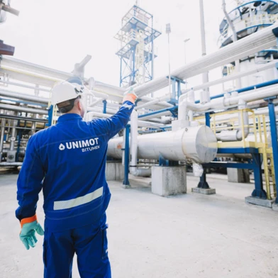 A group of blue-collar workers in engineering workwear from UNIMOT, focused and orderly while handling bitumen. Job crew maintaining cleanliness.